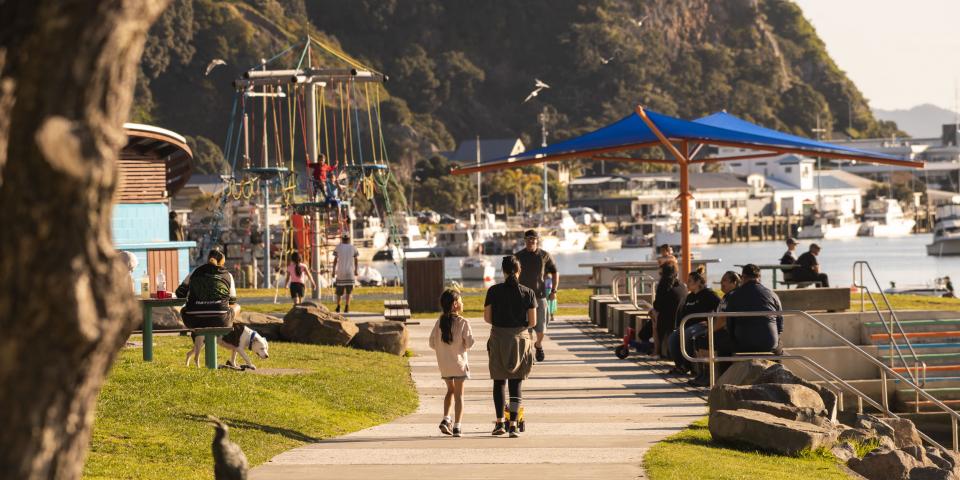 People walking along river with playground in background