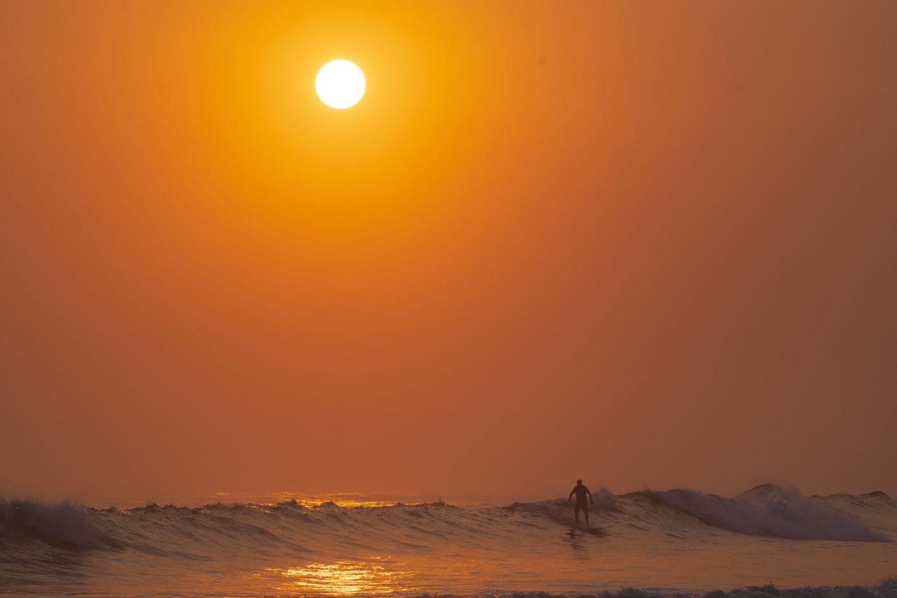 Surfer riding wave at sunrise