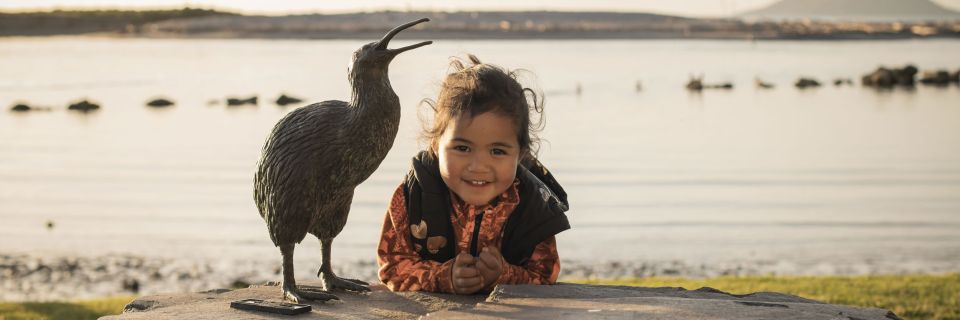 Child standing next to Kiwi statue with Moutohora in background