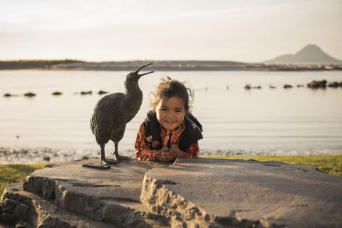 Child standing next to Kiwi statue with Moutohora in background