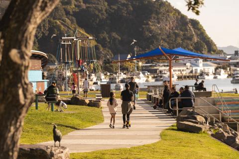 People walking along river with playground in background